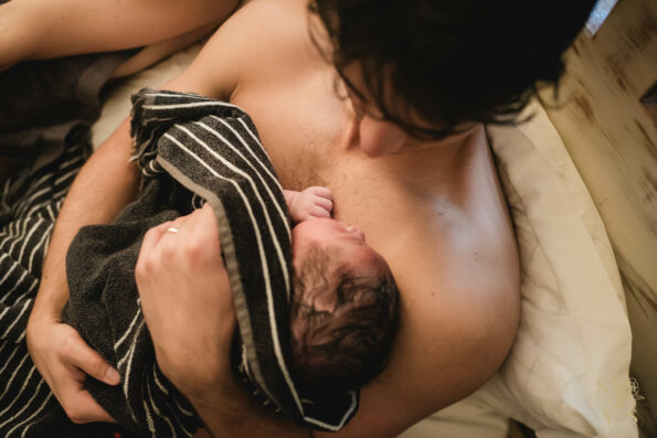 "Joyful moment as a father cradles his newborn for the first time after a water birth, engaging in skin-to-skin contact to foster a precious bond."