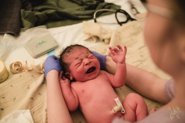 "Newborn expressing vocal vigor while midwife prepares to measure the baby's head, capturing the intense and raw moments of the first cries during a delivery."